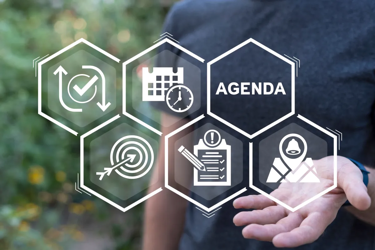 Blick auf Grafik in Bienenwabenform mit fünf Symbolen und einer Wabe, die mit "Agenda" beschriftet ist - im Hintergrund balanciert ein verschwommener Mensch das Gebilde in der offenen Hand